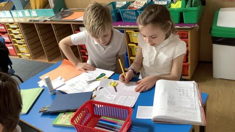 A boy and a girl work together at a table with a box of felt tip pens in front of them