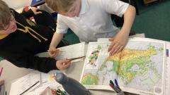 Two children helping each other explore an atlas