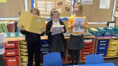 Children are reading from their books near to some drawers in a classroom.