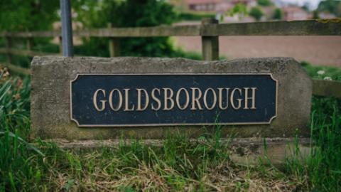 A rock with a dark metal sign attached to it which says Goldsborough in gold capital letters.