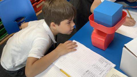 A boy looks closely at the face of a scale.  A large blue block is in the scale tray.