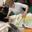 Two children helping each other explore an atlas