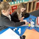Two girls work together on coloured paper labelling a hundred square which has been cut up into sections