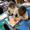 Two children work together on coloured paper labelling a hundred square which has been cut up into sections