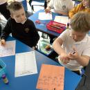 Two children work together solving division questions on coloured paper in felt tip pen