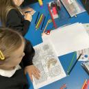 Two girls are colouring in detailed bookmarks.