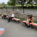 Children sit on multicoloured benches on a school playground.  They are writing.